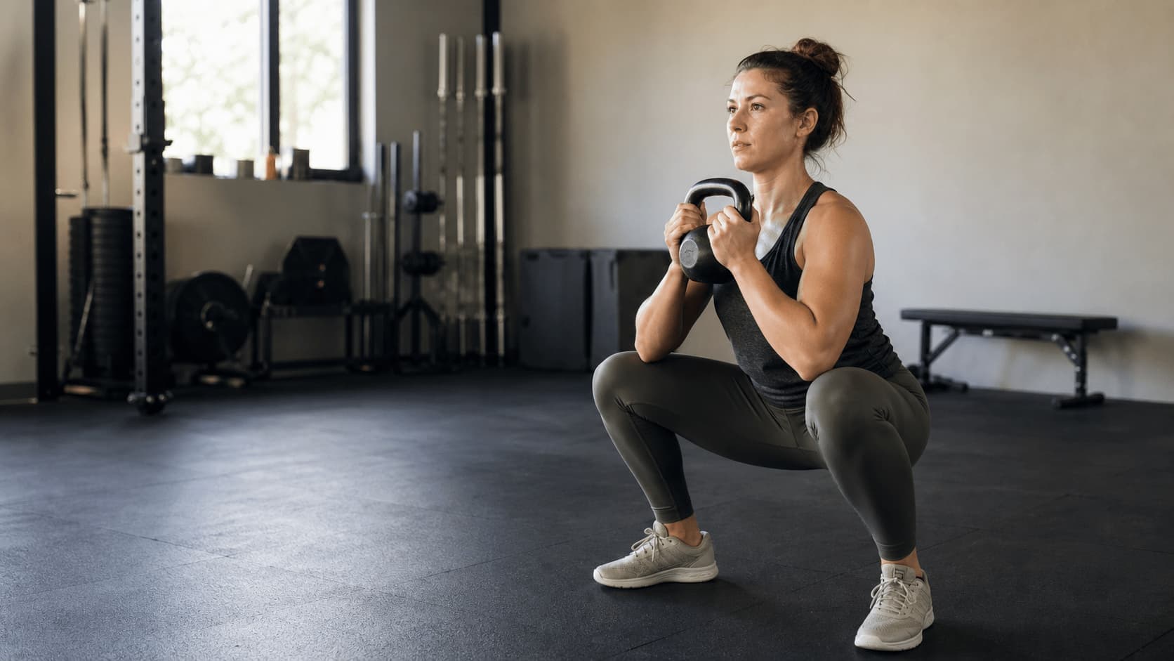 A woman doing a kettlebell squat in a gym.